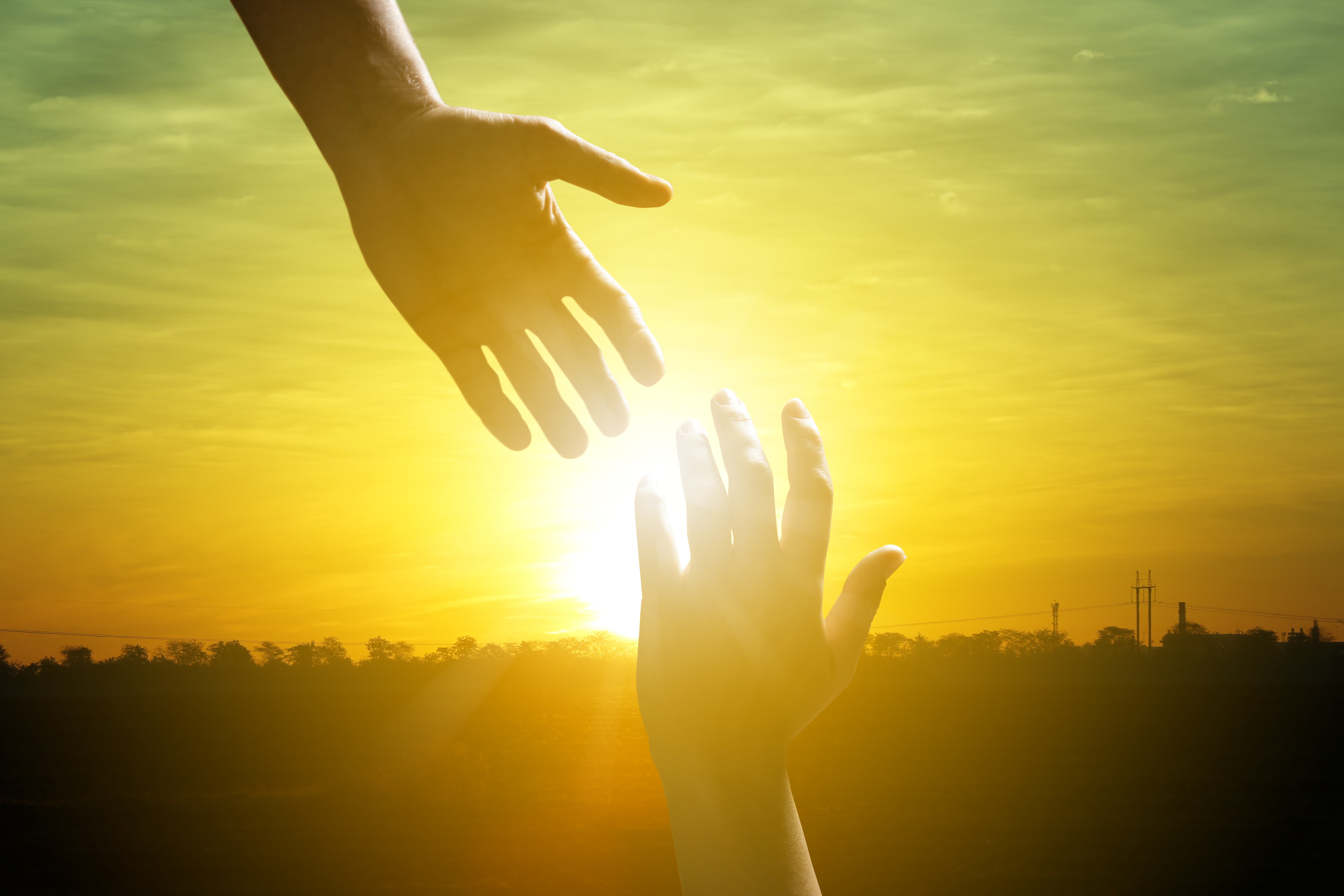 Two hands reaching toward each other against a golden sunset