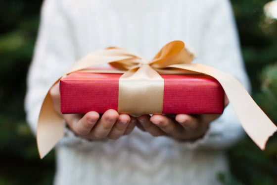 A beautifully wrapped red gift with a gold ribbon being held with care